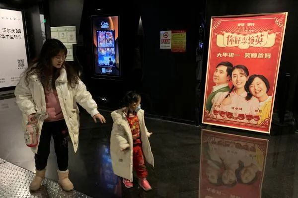 ▲2月19日，在北京一家电影院里，观众从《你好，李焕英》海报旁走过。（图片来源：路透社）