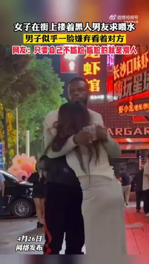 女子在街上搂着黑人男友求喂水，男子似乎一脸嫌弃看着对方……