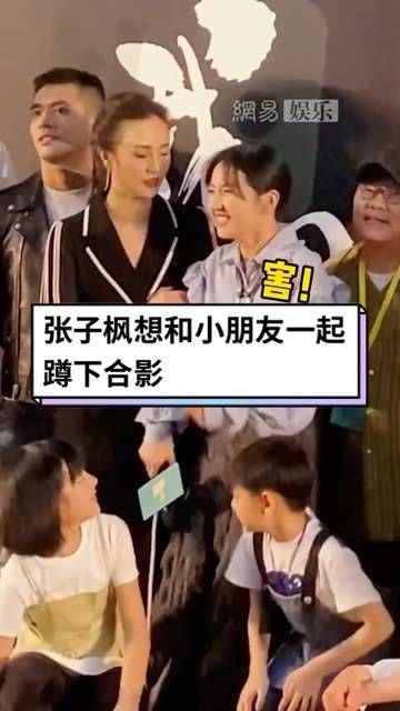 想和小朋友们一起蹲下来合影，却被突然拉住，妹妹不好意思地笑了…