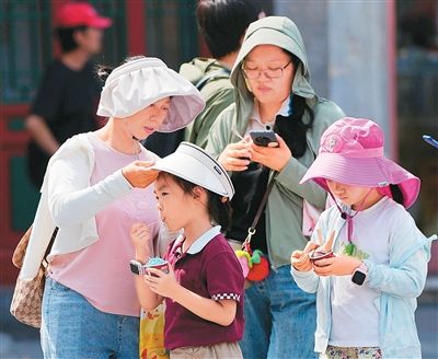 近日，在北京前门大街，游客通过戴帽子、穿防晒服抵挡烈日。 新华社记者 鞠焕宗摄
